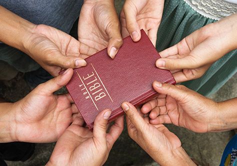 Viele Hände halten gemeinsam am Wort Gottes, der Bibel, fest